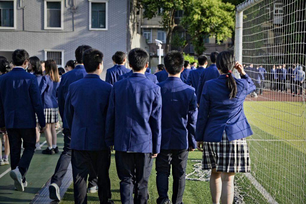 Students in uniform are walking near a sports field.